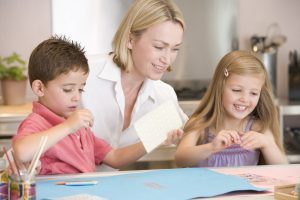 Home-based childcare educator doing a creative learning activity with two young children in a home setting.